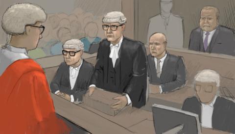 Courtroom sketch showing a legal hearing in progress. A judge in a red robe is seen from behind in the foreground, facing several barristers wearing traditional black robes, white neck bands, and white wigs. One barrister stands at a lectern addressing the court while others are seated nearby. Robert Bush is seated behind a glass partition and other figures are in the public gallery. The image is rendered in a muted palette of grey, brown, and black tones, with the judge’s bright red robe providing a strong visual focal point.