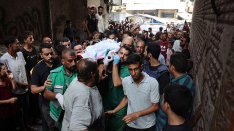 Men carry the body of an Al Jazeera journalist through a narrow street