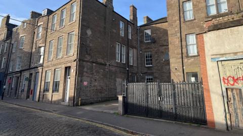 A small car park on a cobbled street surrounded on either side by buildings