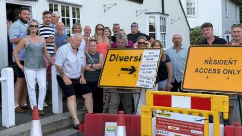 Yellow signs for roadworks outside a pub with several people standing behind them.