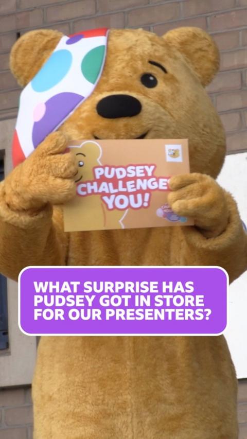 Pudsey, a yellow fluffy human sized bear stands outside holding an envelope which reads 'Pudsey challenges you'