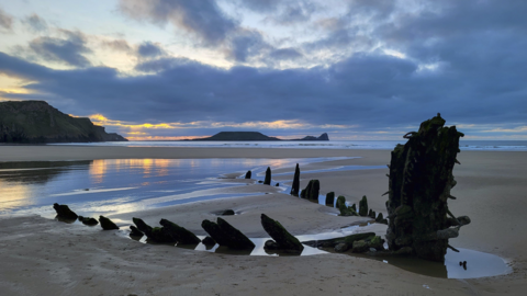 Rhossili beach you can also see the remains of the Helvetia, shipwrecked in 1887 on the sands and visible during low tide, twilight, reflections of the setting sun is visible in the wet sand.