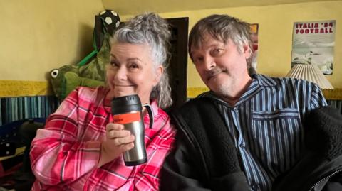 Dawn French sat next to Mark Heap on a sofa. They are smiling at the camera.