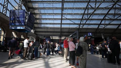 Passengers stand on a concourse at Liverpool Lime Street railway station.