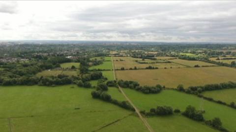 An aerial showing green fields in Oxfordshire, with a road running up the centre of the picture.