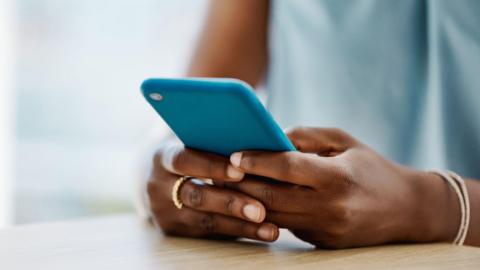 A young hand with gold rings and a gold bracelet holding on to a blue phone.