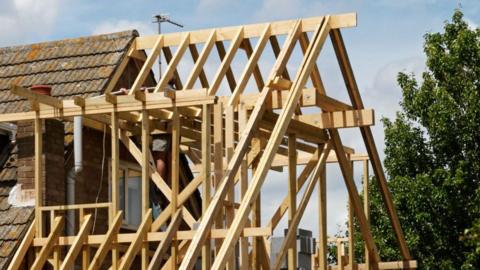 A wooden roof structure being built on to the side of a existing house