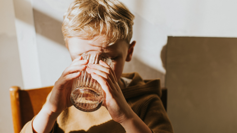 A boy with blond hair drinking from a glass of water