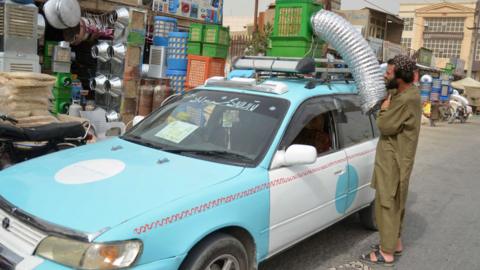 A taxi driver position an air conditioning unit on top of his vehicle.