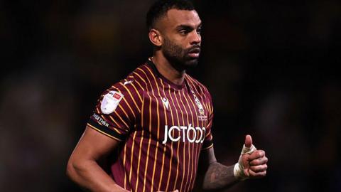 Curtis Tilt in action for Bradford City. He is wearing a maroon and gold striped football shirt with black shorts and socks.