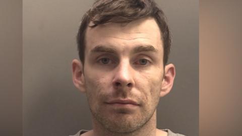 A police mugshot of a man in his 30s with brown hair and blue eyes looking into the camera with a blank expression