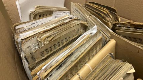 Papers with musical notes stacked into cardboard boxes.