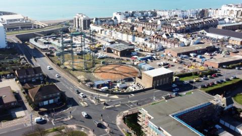 An aerial view of a brownfield site. It is surrounded by terrace housing and a pale blue sea is visible in the background. 