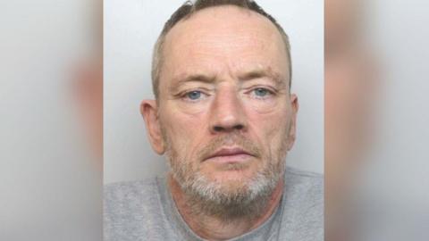 Mugshot of Paul Rowlands. He is wearing a grey shirt and has a grey beard.