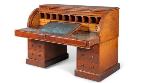 A large mahogany desk, with a row of cubby holes along the top, and a raised, sloped plinth for writing on. Each desk leg has three drawers.