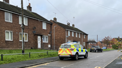 A police car parked streetside in Pentre Gwyn estate in Wrexham in front of semi-detached and block properties with brown brick and white window trim and doors