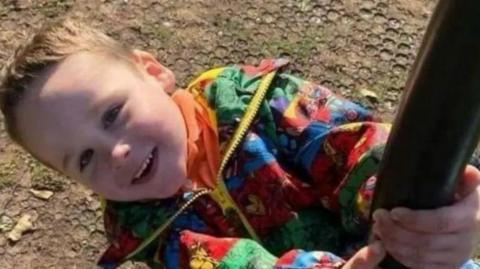 Leo Painter is smiling and wearing a colourful jacket as he swings from a pole