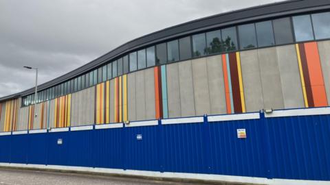 An exterior wall with bands of different colours, including yellow, orange, and burgundy.