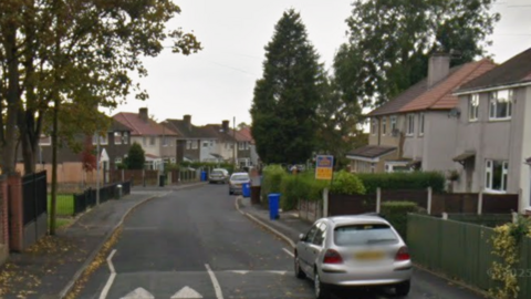Google street view of semi-detached two storey houses lining a road with parked cars and trees.