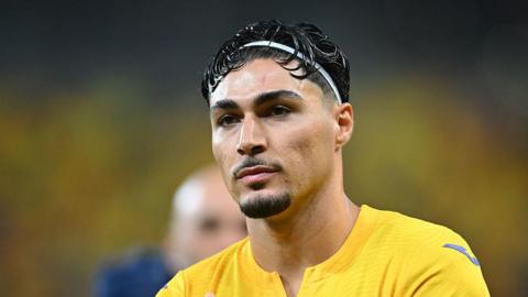 Lisav Eissat walking on the pitch wearing a yellow Romania shirt at the end of a match