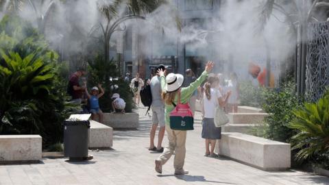 Tourists cool off under a cloud of mist in Valencia, Spain on Sunday