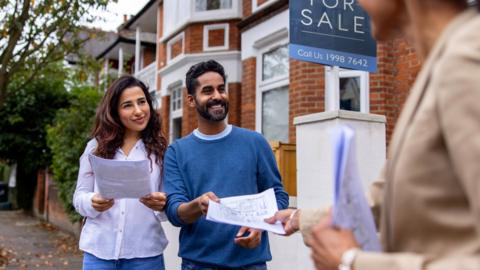 A couple outside a house with a for sale sign