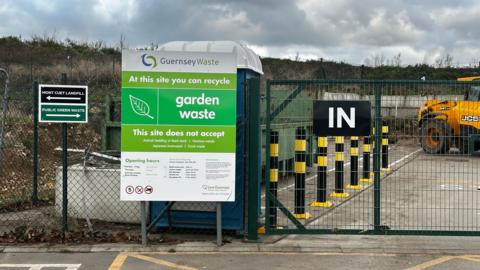 A picture of the entrance to the Mont Cuet site. There is a large green fence with vehicles inside.