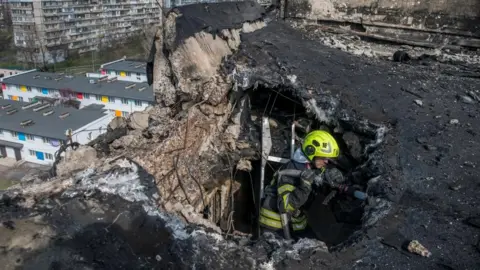 Firefighter emerges from crater on roof of apartment building in Kyiv, following a drone strike.