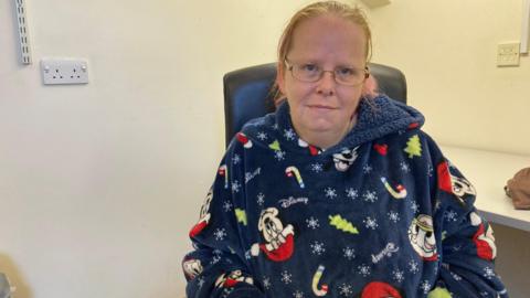 A woman with blonde hair tied back is wearing a navy blue onesie with Mickey Mouse on it.