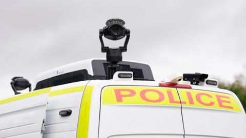 Top of a white police van with a black camera attached on it.