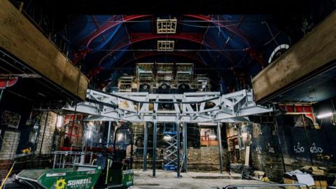 Steel girders elevated over a stage area in a large arched hall