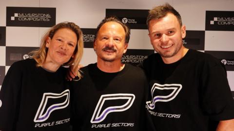 Jennie Gow, Neil Cole and Chris McCarthy, standing arm in arm in front of black and white chequered branding, are in black tops with purple logos that spell out PURPLE SECTORS.
