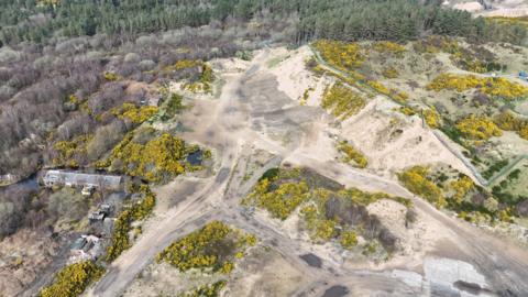 An aerial drone shot of sand dunes and greenery. Work has clearly taken place on the site.