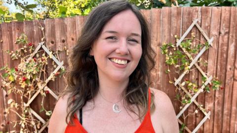 A white woman with brown hair and an orange top smiles at the camera