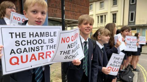 Children in school uniform hold signs saying "The Hamble School is against the quarry"