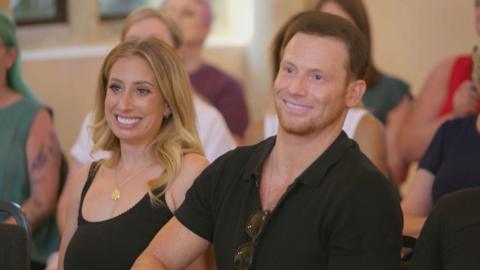 Stacey and Joe, sitting down in an audience, smiling at the stage. Stacey wears a black strapped top, Joe wears a black shirt.