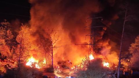 A large fire at night-time with orange flames and power cables