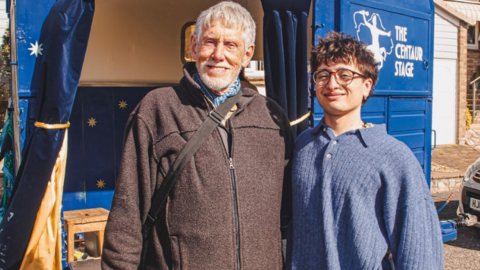 A young man stood next to his grandad in front of an old horsebox which has been converted into a stage 