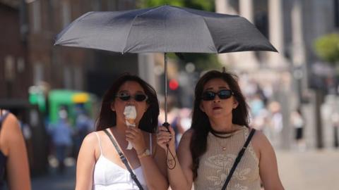 People shield from the sun under an umbrella, on the Millennium Bridge in London