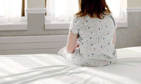 Child sits with back turned on bed. Stock image.
