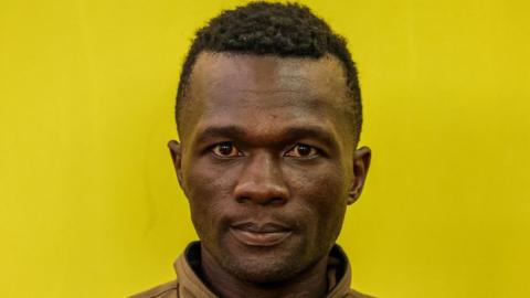 Kenyan suspect Collins Jumaisi Khalusha stands against a yellow wall in court