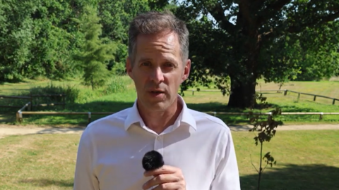 A man wearing a white shirt is standing at a park.