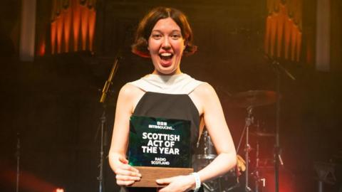 Alice Faye wearing a black and white dress holding the trophy for BBC Introducing Scottish Act of the Year.