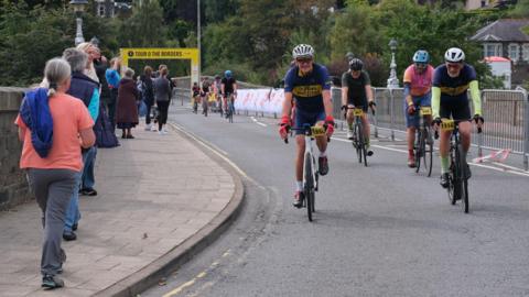 A number of cyclists crossing the finish line in Peebles on the Tour O The Borders - some spectators are lining the route
