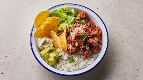 A bowl with beans, lettuce, avocado, white rice and corn chips.