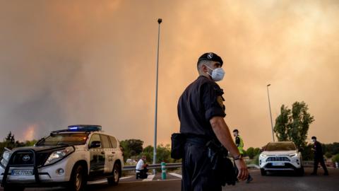 A Civil Guard officer wears a protective mask as smoke from a wildfire obscures the sky in Cenicientos, Madrid