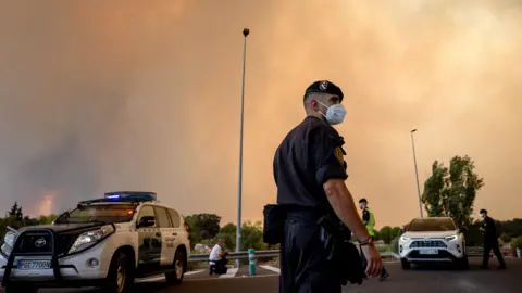 A Civil Guard officer wears a protective mask as smoke from a wildfire obscures the sky in Cenicientos, Madrid