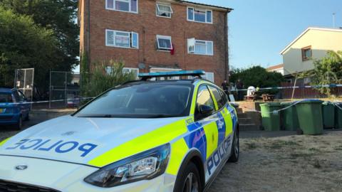 A police car is parked in front of a three-storey brick building on Weston Lane, in Southampton.