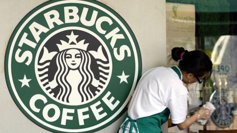 A Starbucks employee seen outside a branch in South Korea. A large Starbucks Coffee sign can be seen in the photograph.
