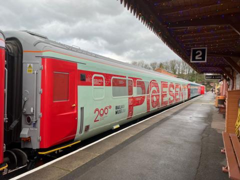 A train carriage parked up at a railway station. The words 'present' are written on the train carriage as well as '200 Railway Museum'